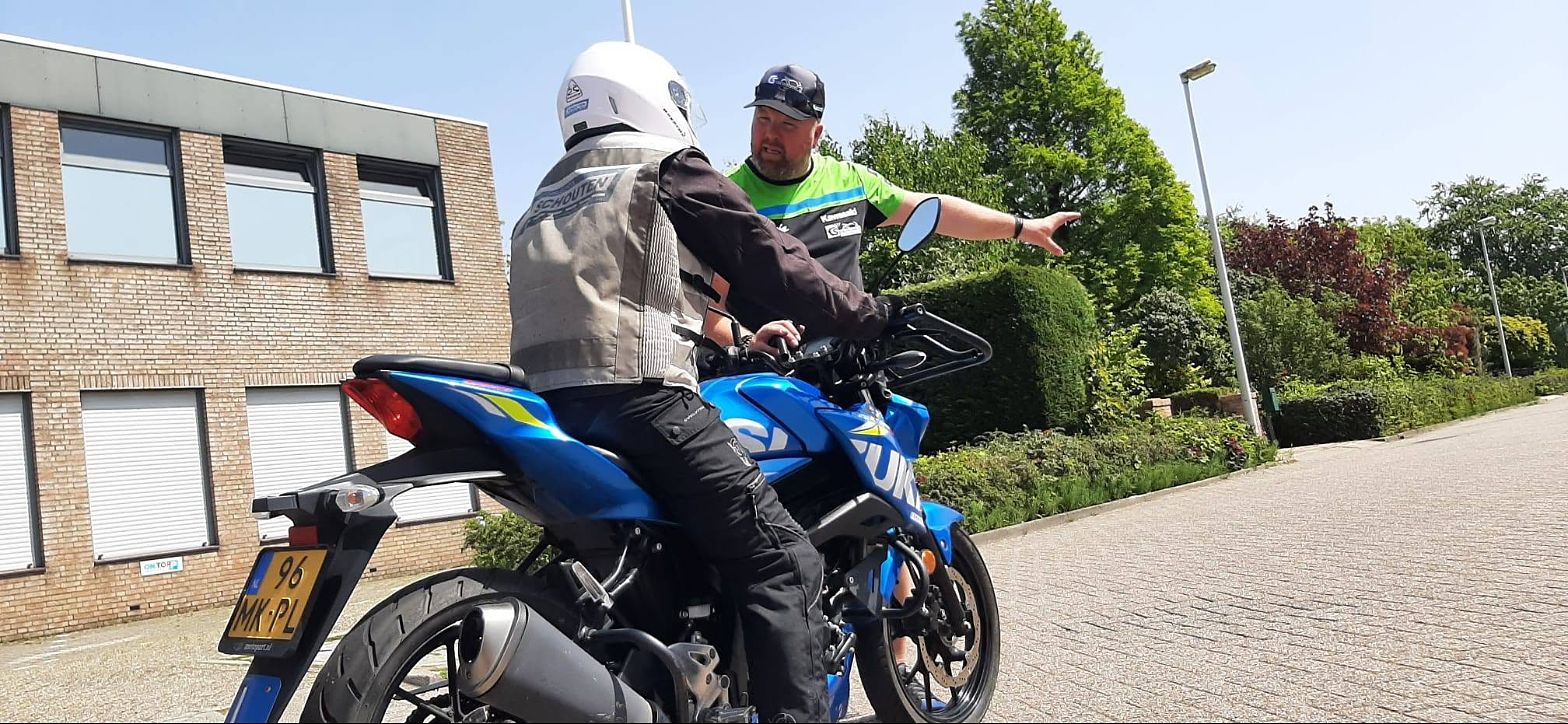 Duncan wijst een leerling op de blauwe Suzuki de weg tijdens een les